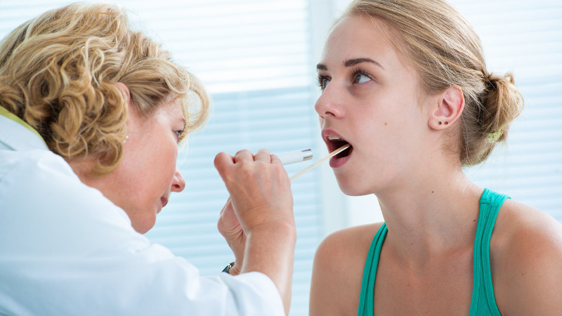 Doctor checking with depressor sore throat to teenage girl
